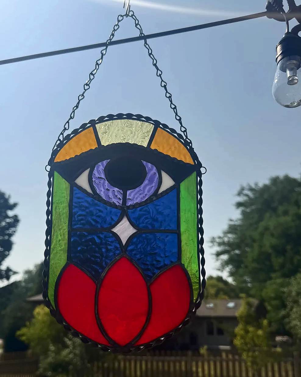 All-seeing eye stained-glass suncatcher above a red lotus, with daylight colors and a dark starry sky