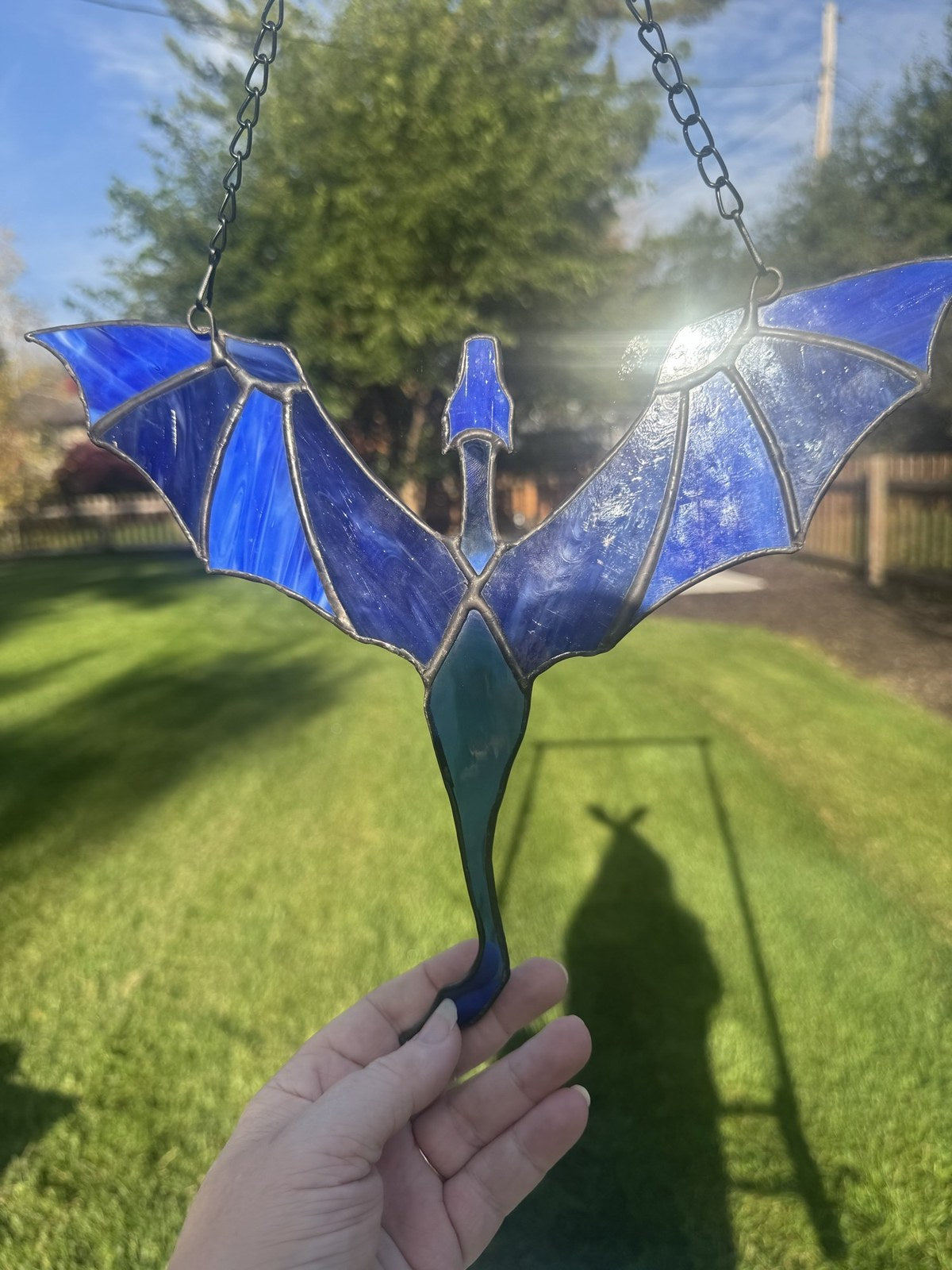 Dragon in Flight stained glass suncatcher in blue, held up in the sun