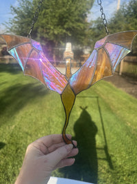 Dragon in Flight stained glass suncatcher in gold with iridescent wings, held up in the sun