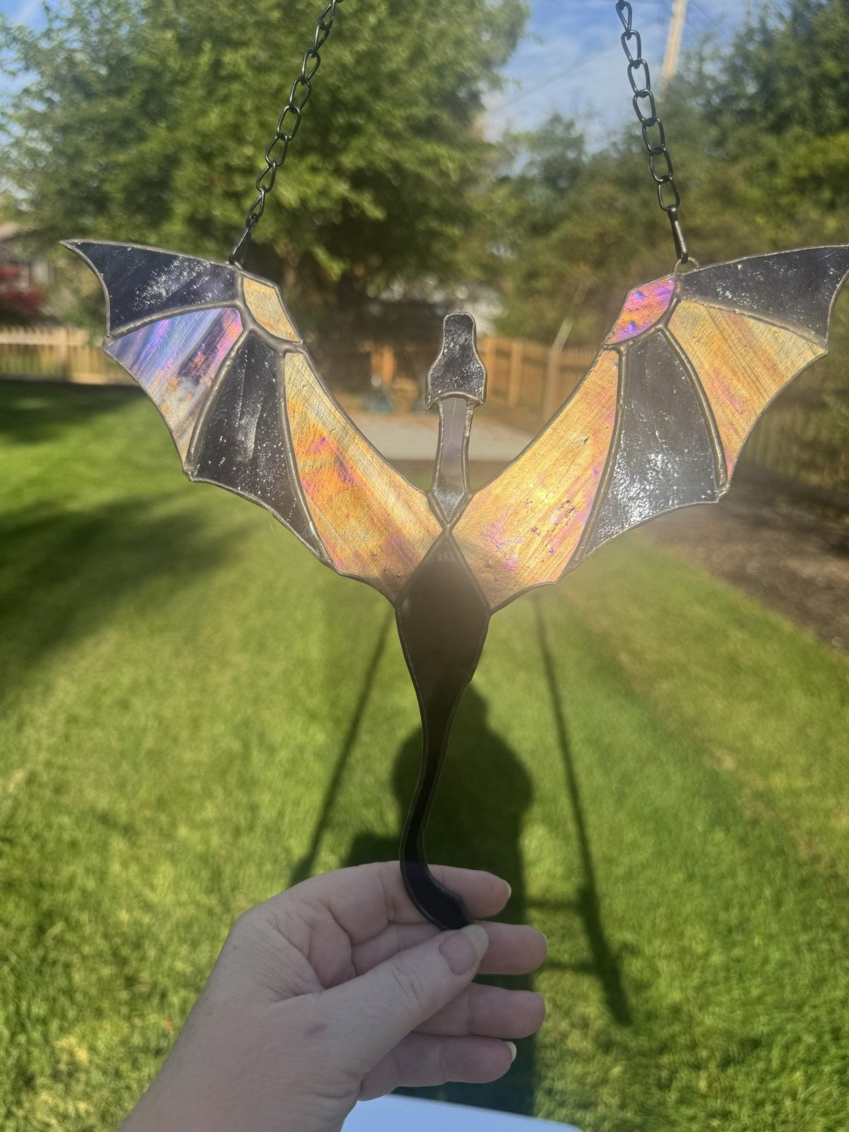 Dragon in Flight stained glass suncatcher in purple with iridescent wings, held up in the sun