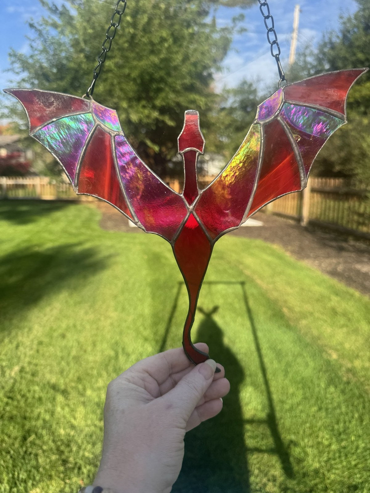 Dragon in Flight stained glass suncatcher in red with iridescent wings, held up in the sun