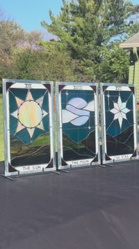 The Sun, The Moon and The Star stained-glass panels in outdoor light, showing the iridescent central glass and included stands.