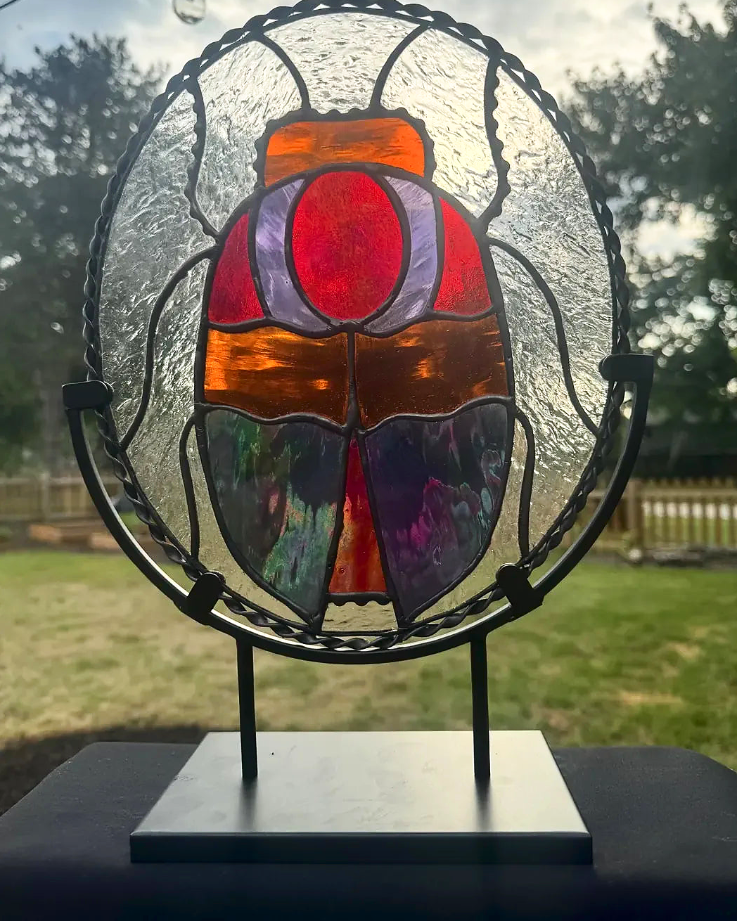 Standing iridescent stained-glass scarab in red, purple, and orange, on a round black metal stand