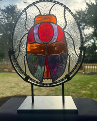 Standing iridescent stained-glass scarab in red, purple, and orange, on a round black metal stand