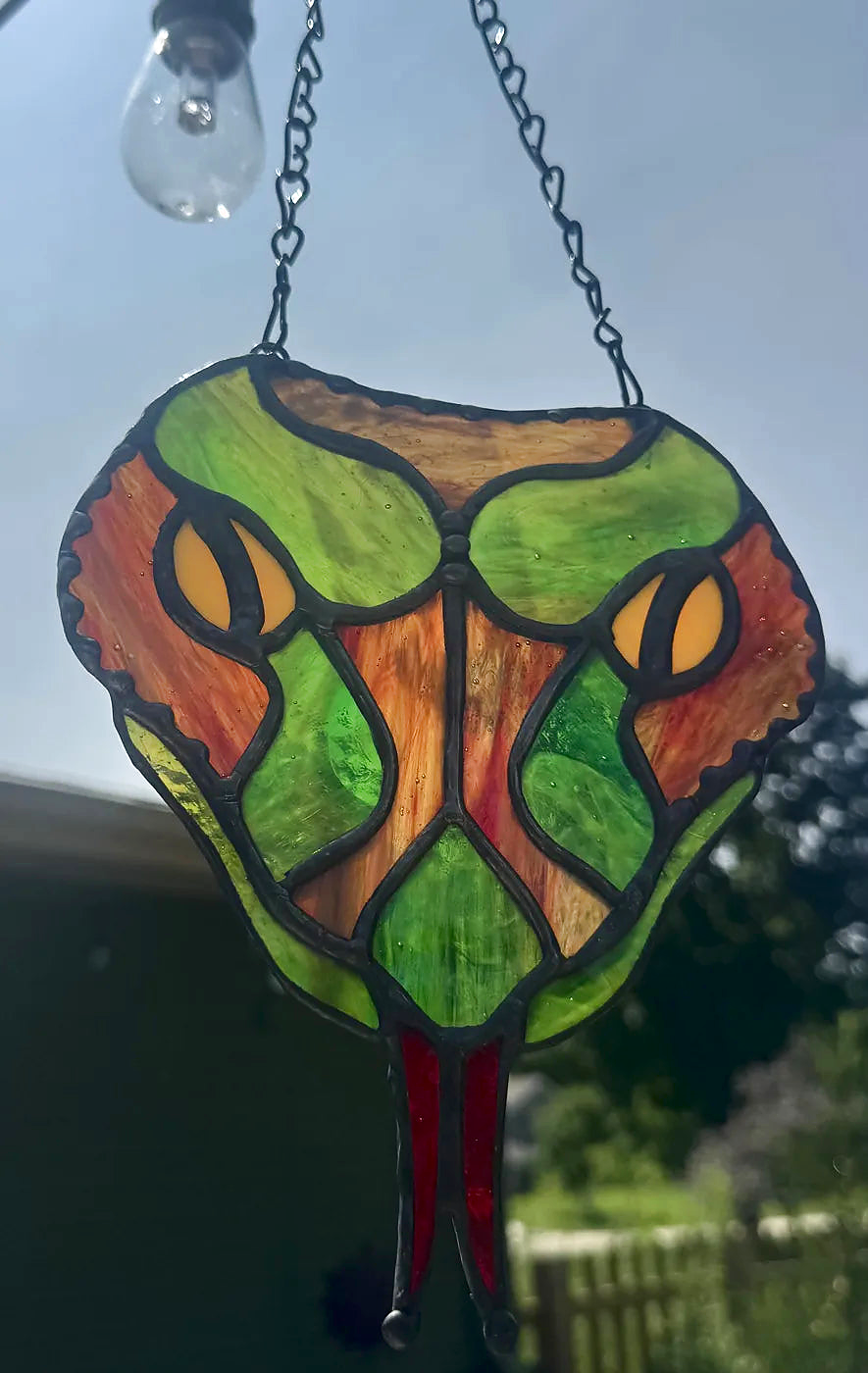 Brown snake-head stained-glass suncatcher with yellow eyes and forked red tongue