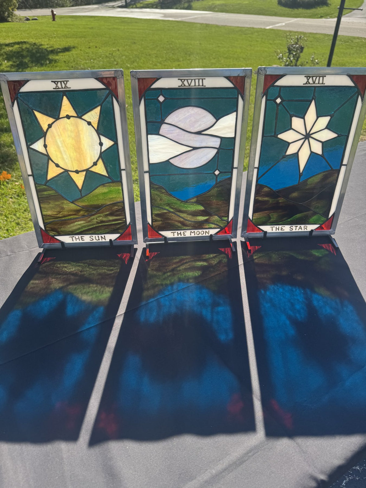The Sun, The Moon and The Star stained-glass tarot panels together in sunlight, casting blue, green and red reflections onto the table.