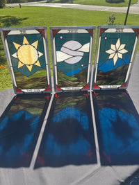 The Sun, The Moon and The Star stained-glass tarot panels together in sunlight, casting blue, green and red reflections onto the table.
