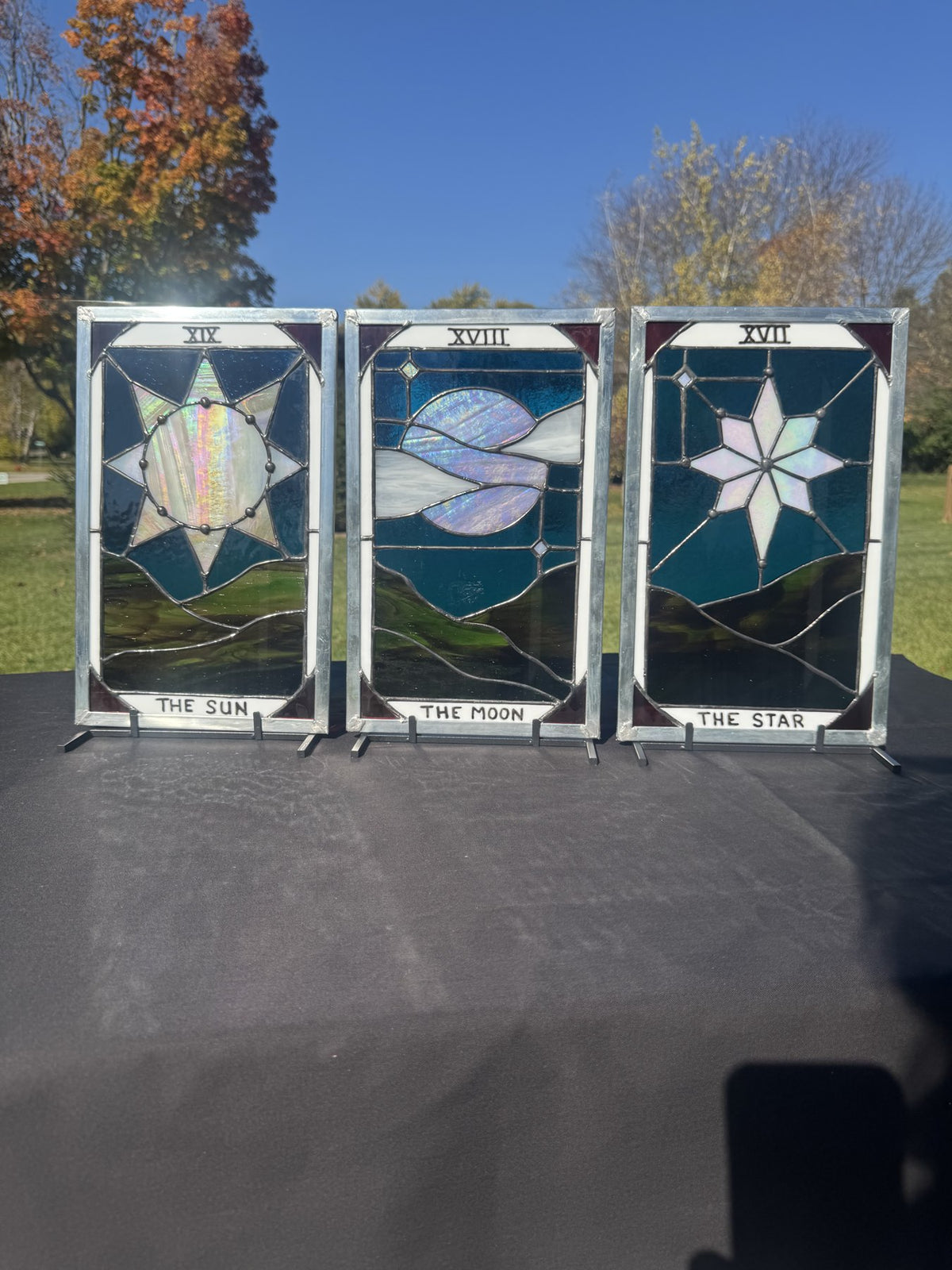 The Sun, The Moon and The Star stained-glass tarot panels displayed together outdoors, showing their iridescent glass and included stands.