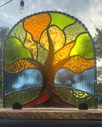 Standing autumn tree stained-glass panel in green, gold, and orange, displayed on a wood stand
